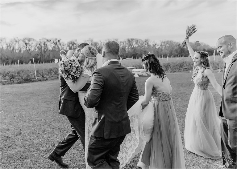 bride and groom hug after ceremony as wedding party cheers at Ever After Farms wedding