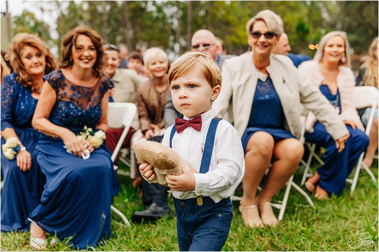 ring bearer looking concerned as he comes down aisle at lakefront wedding