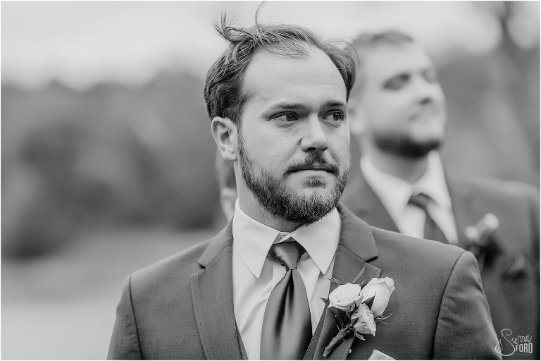 groom sees his bride coming down aisle with tears in his eyes at lakefront wedding ceremony