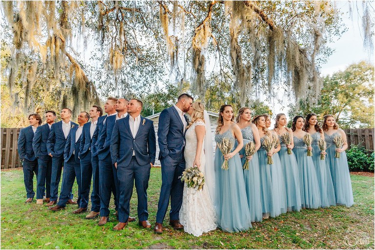 bride and groom kiss as wedding party surrounds them on either side at Ever After Farms wedding