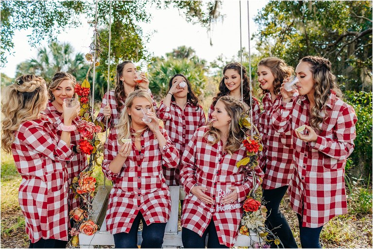 bride takes celebratory shot with bridesmaids in matching plaid button ups before Ever After Farms wedding