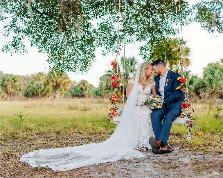 bride and groom nuzzle noses sitting on tree swing together at Ever After Farms wedding