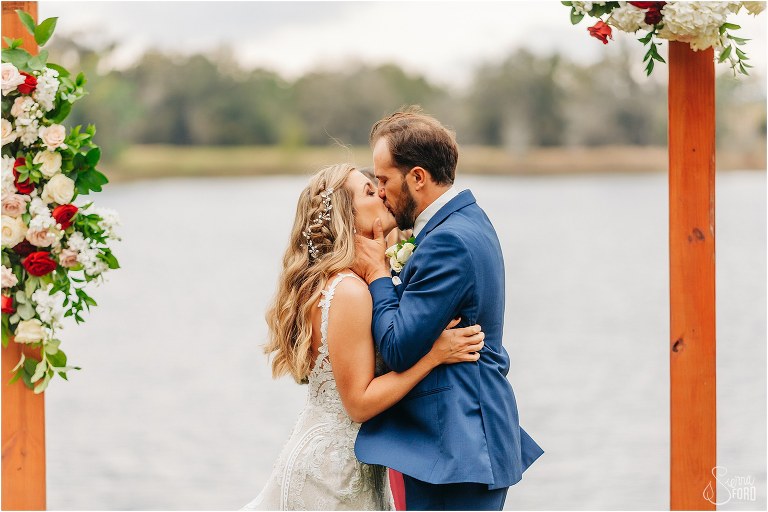 bride and groom share first kiss as husband and wife at lakefront wedding ceremony
