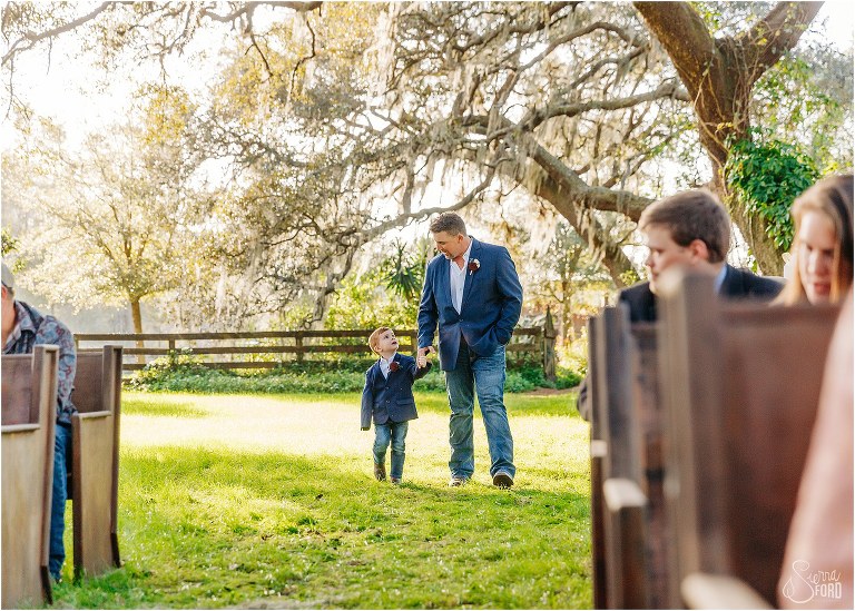 groom and son walk hand in hand down aisle at Isola Farms wedding ceremony