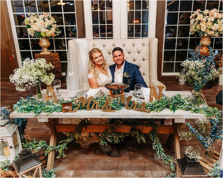 bride and groom pose sitting on love seat at sweetheart table at Ever After Farms wedding