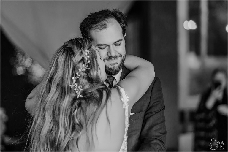 groom smiles as bride nuzzles him during their first dance at lakefront wedding reception