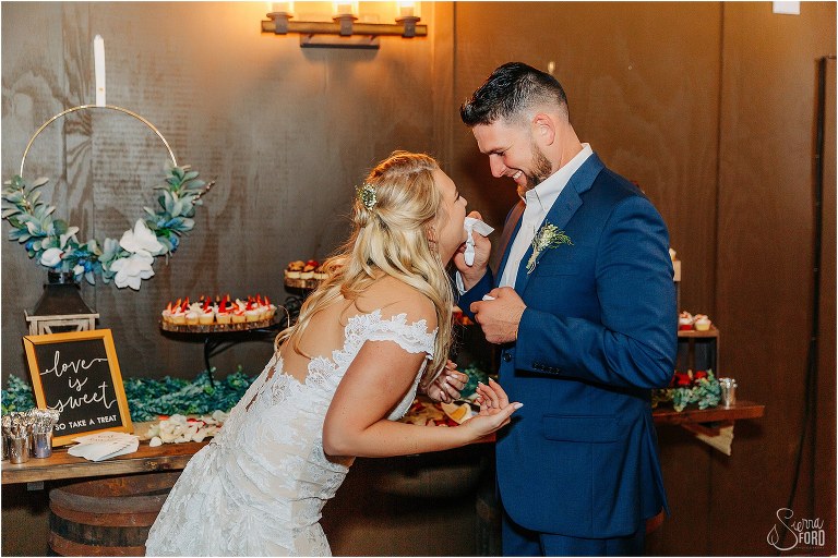 bride laughs as groom wipes frosting off her lips at Ever After Farms wedding