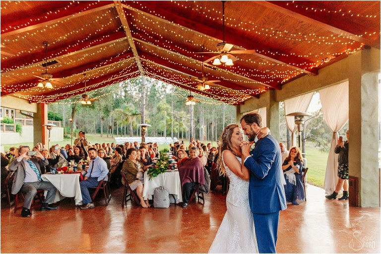 loved ones look on as bride and groom share first dance at lakefront wedding reception