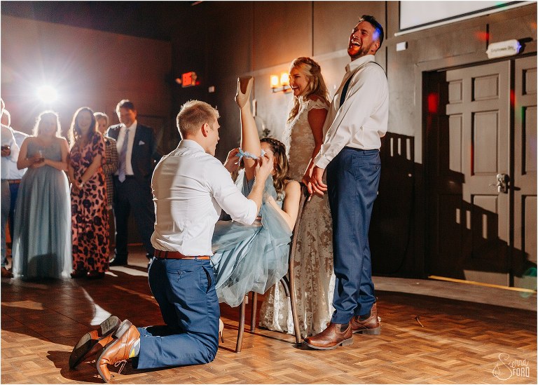 bride and groom laugh as friend replaces garter on the woman who caught bouquet at Ever After Farms wedding