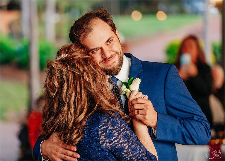 groom smiles as he shares dance with his mother at lakefront wedding