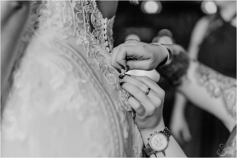 bridesmaid helps button up bride's Martina Liana wedding gown before lakefront wedding