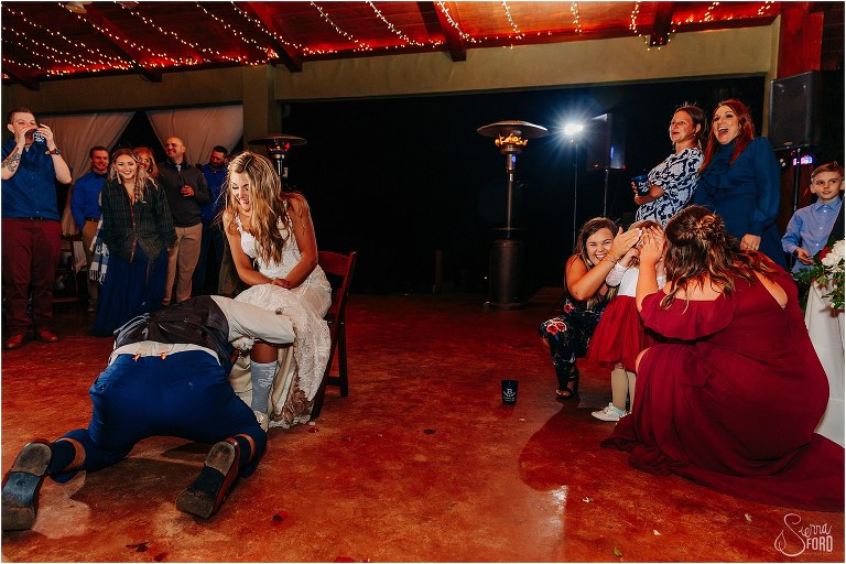 bridesmaids cover flower girls eyes as groom retrieves garter at lakefront wedding reception