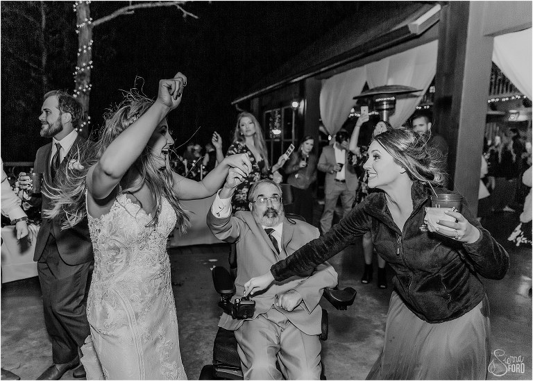 matron of honor steers the wheelchair of the bride's father so he can dance with bride at lakefront wedding