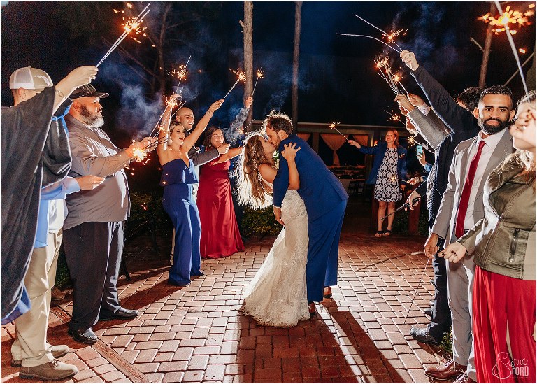 groom dips bride and kisses her during sparkler exit at lakefront wedding