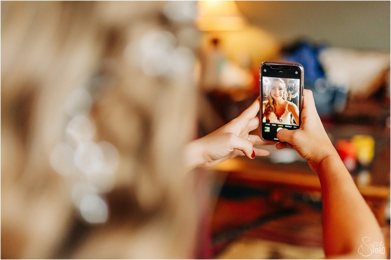 bride takes selfie of finished product before lakefront wedding