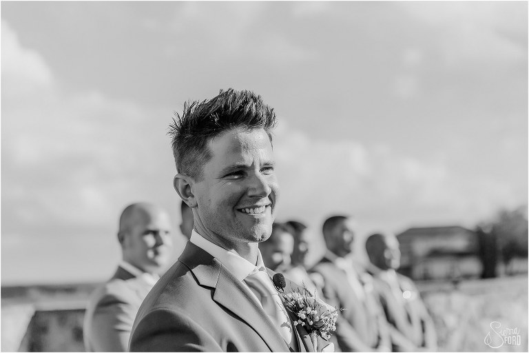 groom beams as he sees his bride come down aisle at Bella Collina wedding ceremony