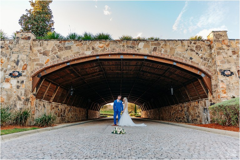 bride and groom stand together under giant brick bridge at Bella Collina wedding