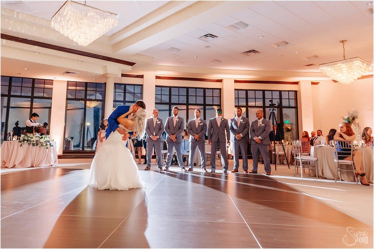 groom dips bride into kiss during first dance surrounded by wedding party at Bella Collina wedding
