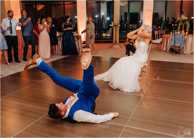 bride hides her face as groom shows off fresh split in his pants during garter retrieval at Bella Collina wedding