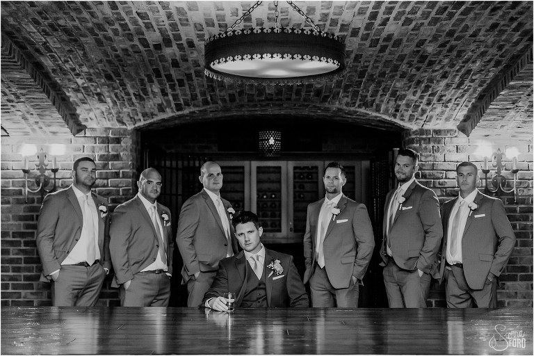 groom and groomsmen share a drink in wine cellar before Bella Collina wedding