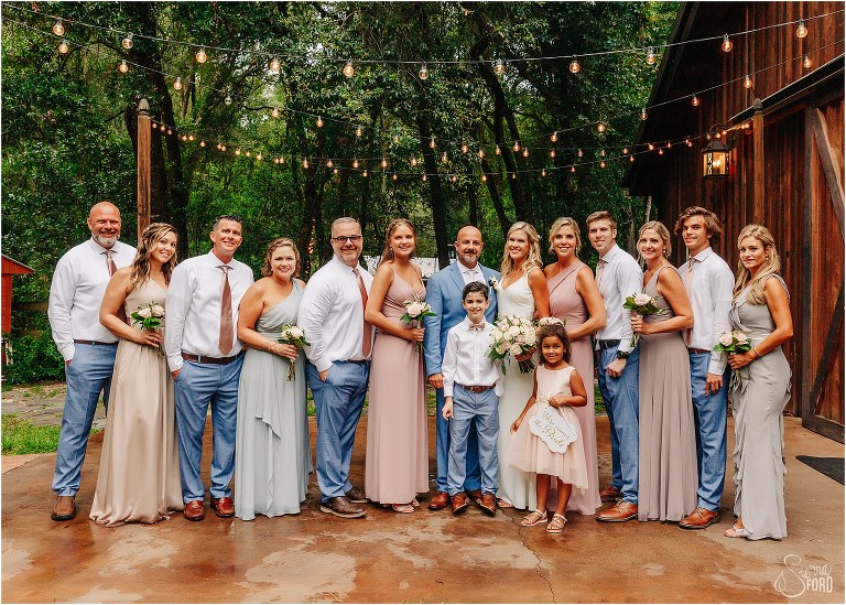bride and groom smiling surrounded by their wedding party in light blue and pastel pink accessories at rustic barn wedding