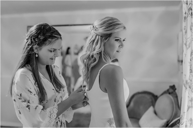 bride's daughter zips up wedding gown before rustic barn wedding