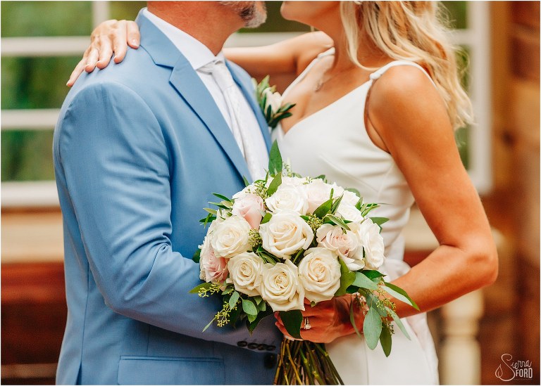 closeup of blush rose bridal bouquet as bride and groom almost kiss at rustic barn wedding