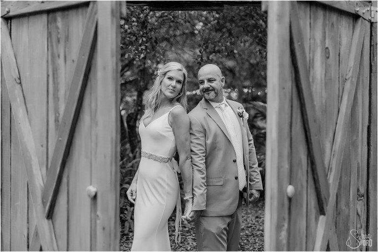 bride & groom stand back to back holding hands as wooden double doors open at rustic barn wedding