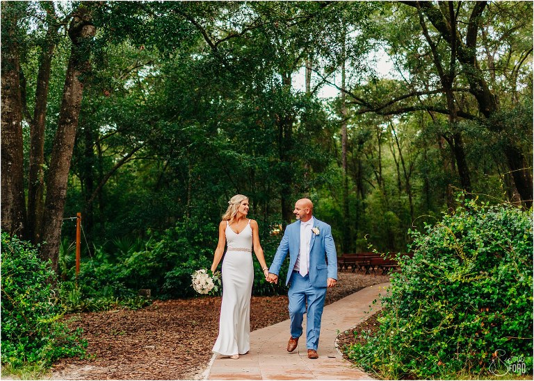bride & groom stroll hand in hand down brick path at rustic barn wedding