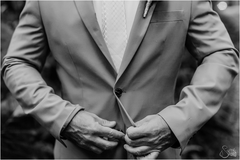 groom buttons up blue suit before rustic barn wedding