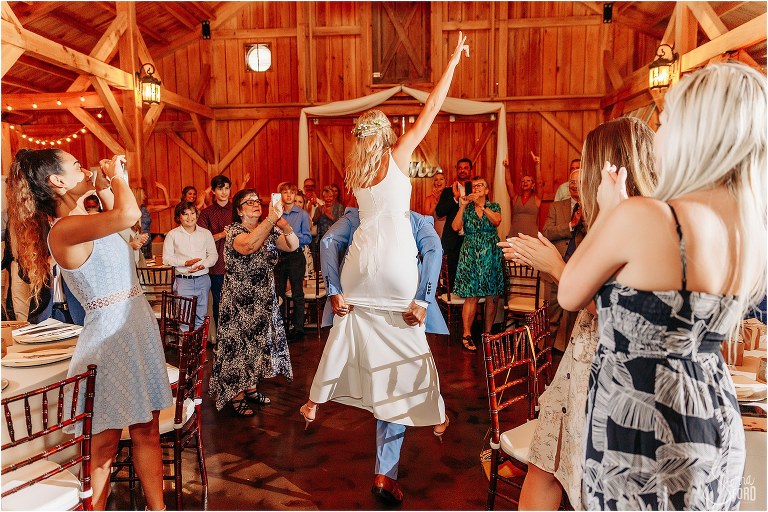 groom gives bride a piggy back ride into rustic barn wedding ceremony