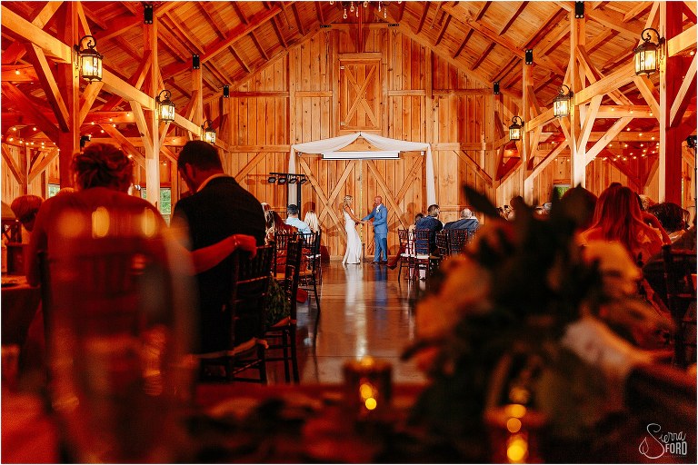 friends & family look on as bride & groom share first dance as during rustic barn wedding reception