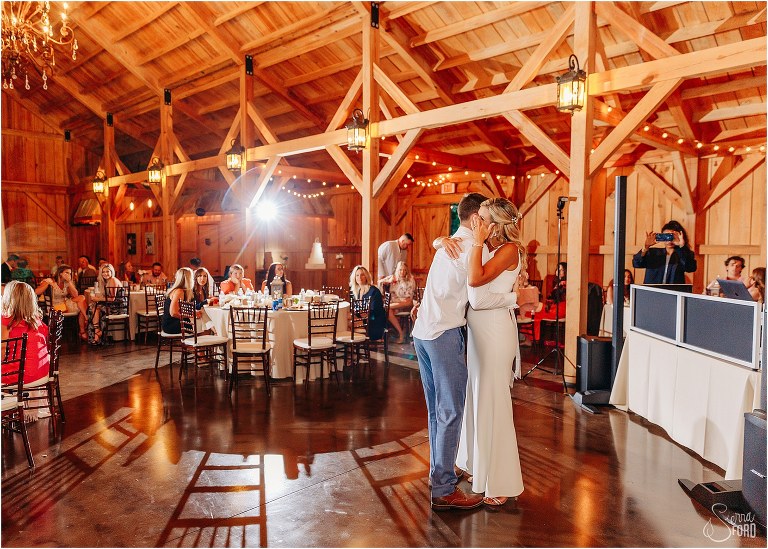bride wipes tear from her eyes as she shares dance with one of her sons at rustic barn wedding
