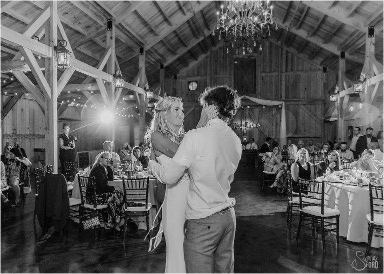bride holds son's face in her hands as they dance together at rustic barn wedding
