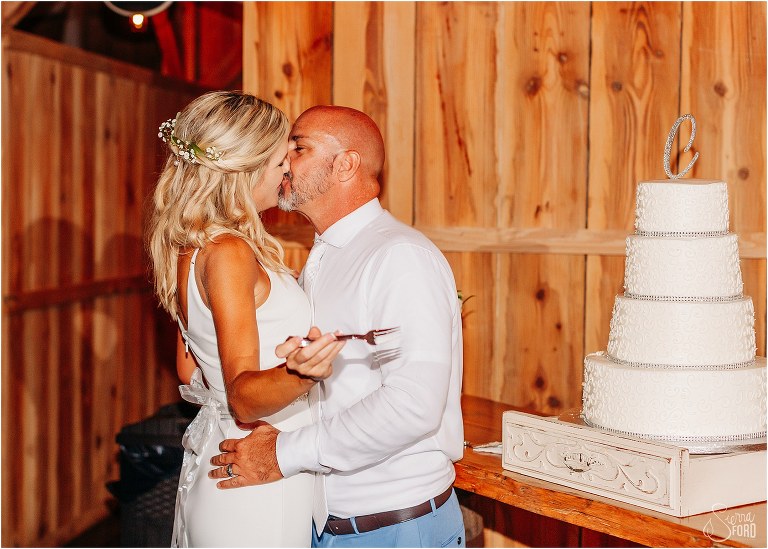bride and groom share a frosting-covered kiss after cutting the cake at rustic barn wedding