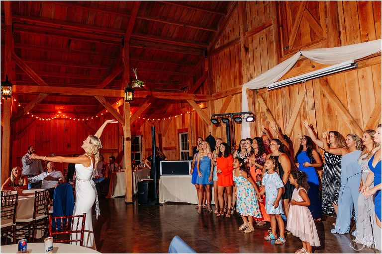 all the single ladies reach for the sky as the bride tosses her bouquet at rustic barn wedding