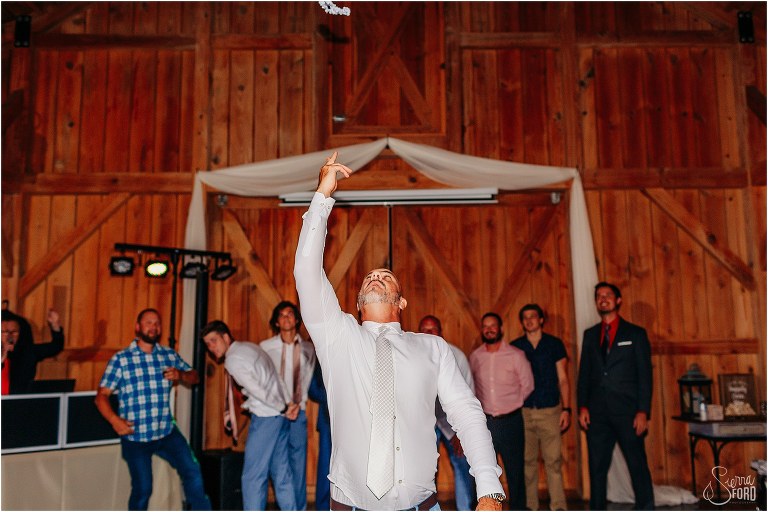 groom tosses bride's garter to all the single men at the rustic barn wedding