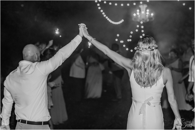 bride and groom cheer hand in hand and look back at their guests after sparkler exit at rustic barn wedding