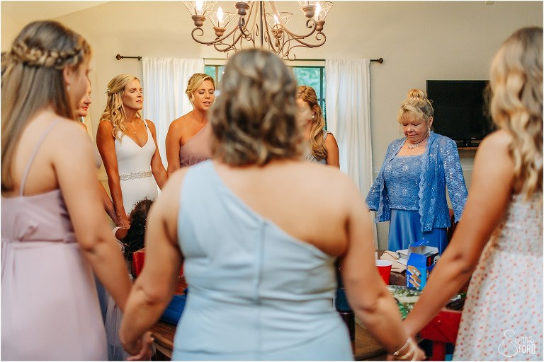 maid of honor leads prayer circle with other bridesmaids before bride's rustic barn wedding