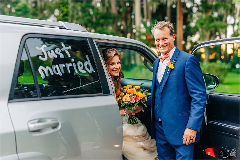 groom helps bride into car with "just married" written on the windows at Kraft Azalea park wedding