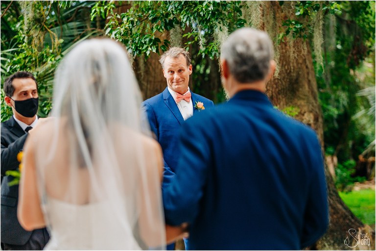 a peek at the surprised groom as his bride walks down aisle with father at Kraft Azalea park wedding