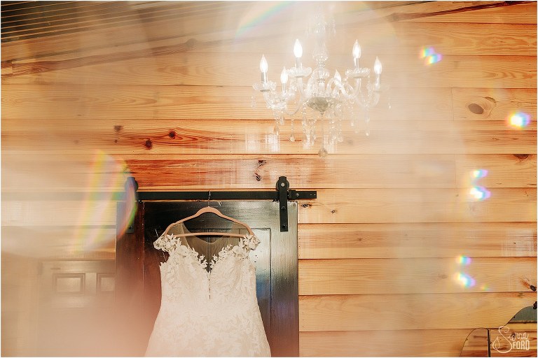 bride's wedding gown hangs on barn door as seen through chandelier crystals at rustic Apopka wedding