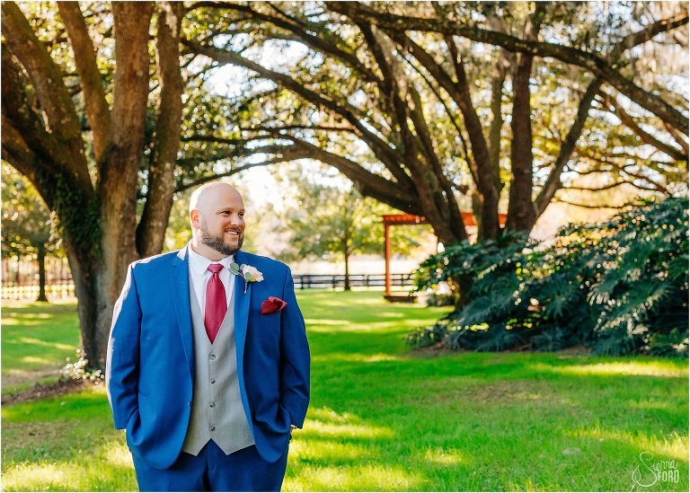 groom looks off in distance as he stands under live oaks at rustic Apopka wedding