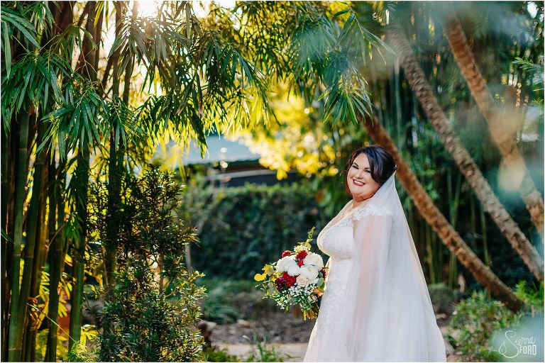 bride grins as sun beams down through greenery in the garden before Apopka wedding venue