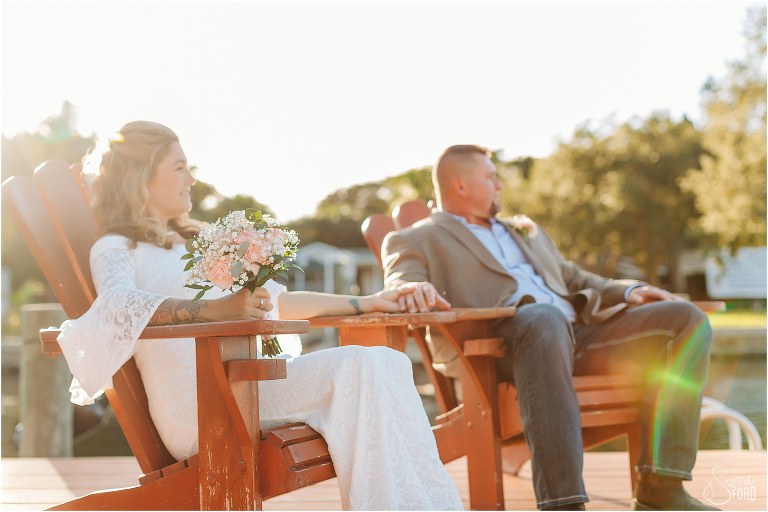 bride and groom hold hands as they look out at river sitting on dock at St. Pete backyard wedding