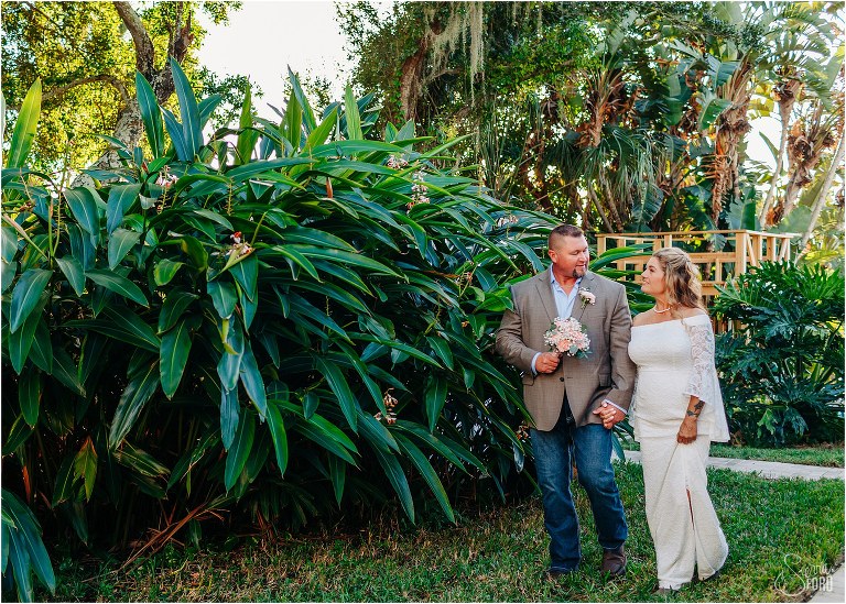 bride & groom walk hand in hand through lush greenery at St. Pete backyard wedding
