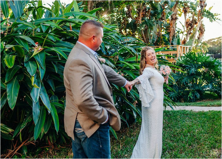 bride laughs as she leads groom through lush greenery at St. Pete backyard wedding