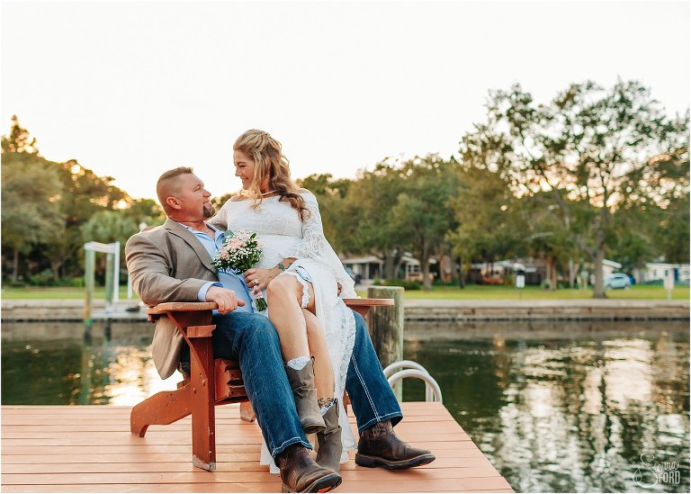 bride looks lovingly at groom sitting on his lap on the dock at St. Pete backyard wedding