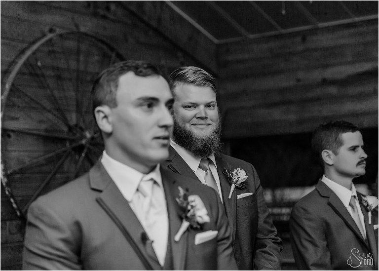 best man smiles as groom watches bride walk down aisle at Hidden Barn wedding