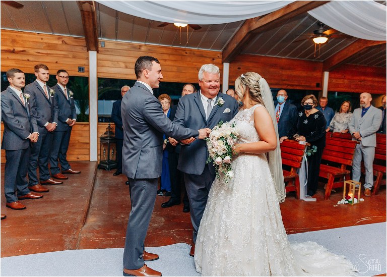 father smiles at bride as he hands her off to groom at Hidden Barn wedding